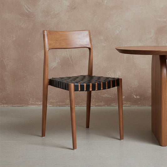 Raw Materials Freya eetkamerstoel met zwart leren zitting en massief teakhouten frame, vanuit een lichte hoek gefotografeerd